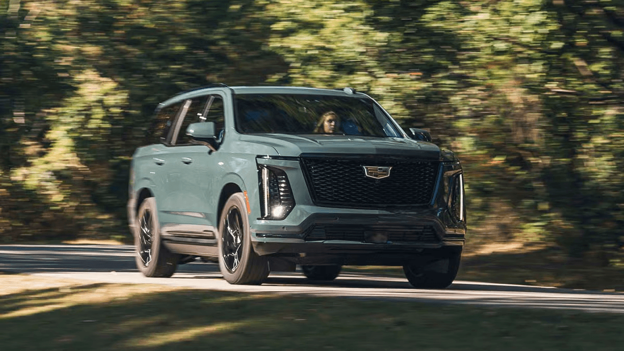 Egy világoszöld Cadillac Escalade luxusterepjáró halad egy erdős úton, elmosódott háttérrel.