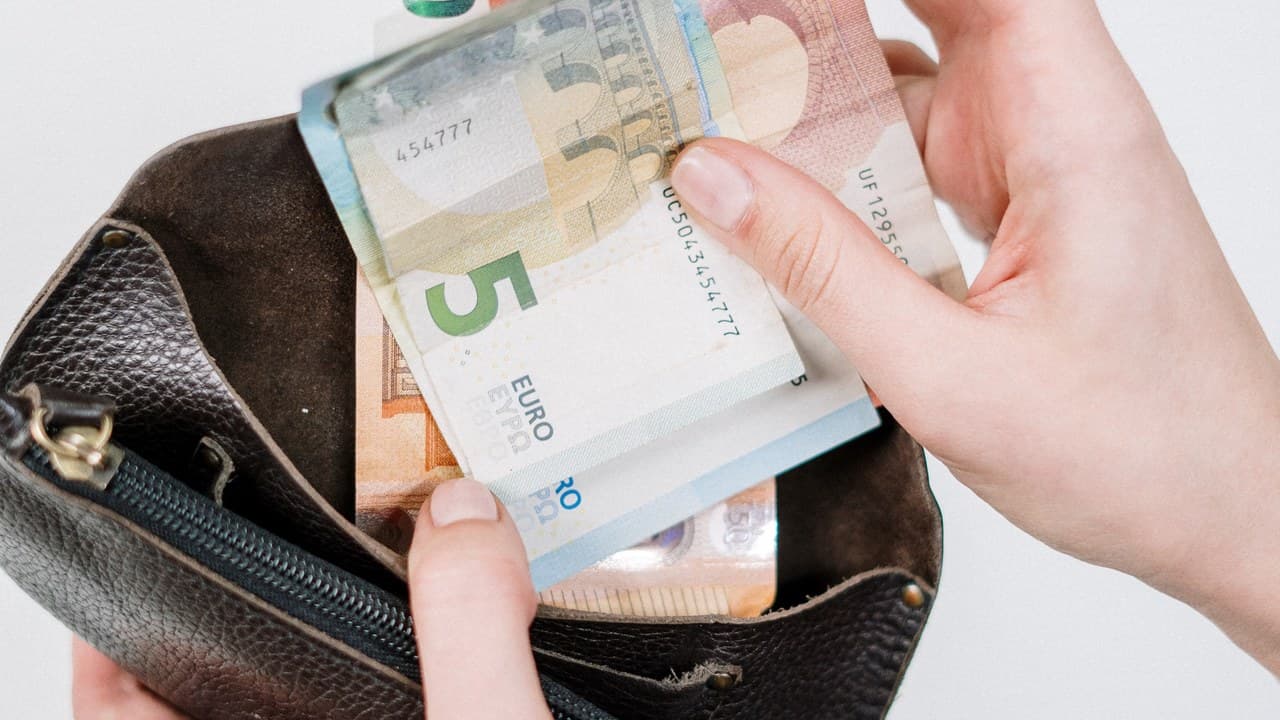 Egy figura adókönyvekkel és euróval teli pénzeszsákkal, a vagyonadó és euróbevezetés témájában. – 2. kép