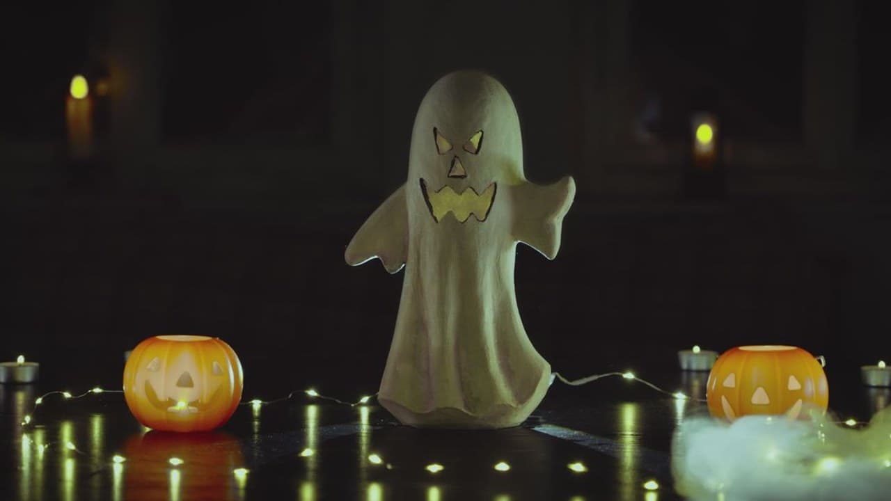 Halloween dekoráció egy világító szellemmel, töklámpásokkal és fényfüzérrel sötét háttér előtt.