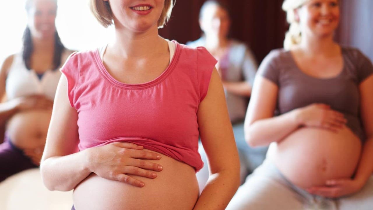 Terhes nők mosolyogva tartják a hasukat egy szülésfelkészítő tanfolyamon.