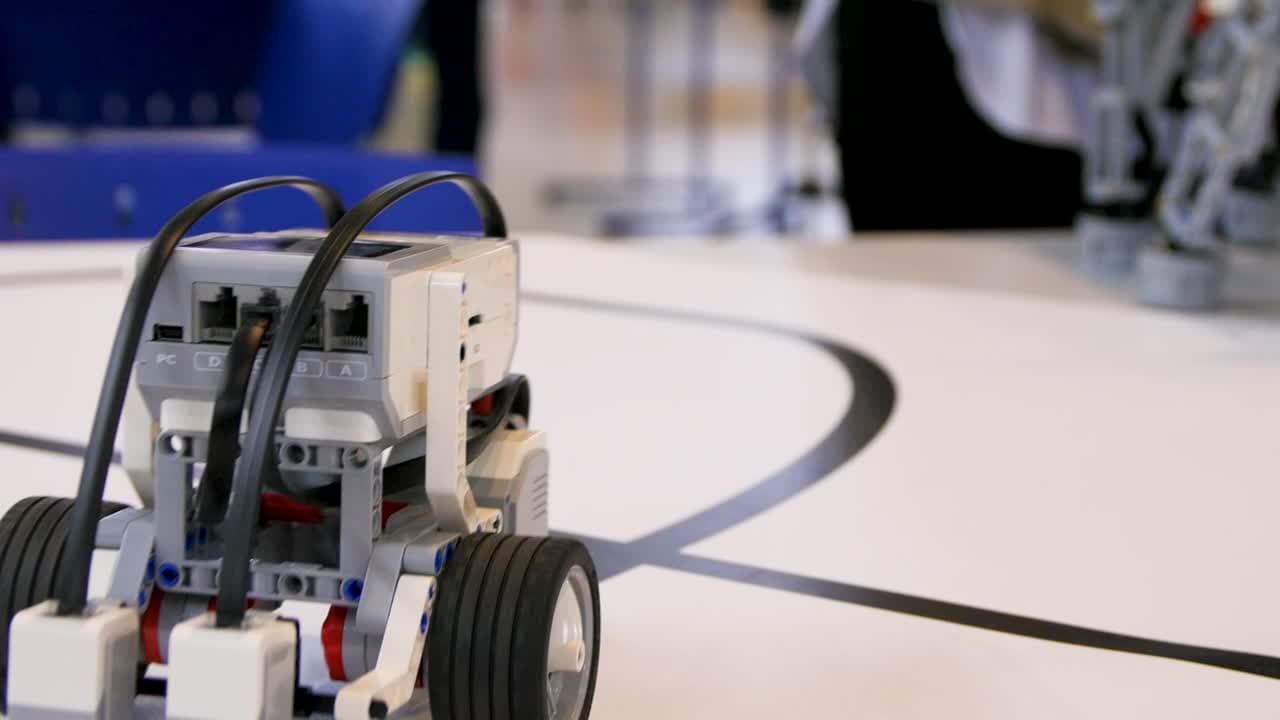 Egy kis robot egy fehér pályán fekete vonalakkal, valószínűleg egy tudományos eseményen.