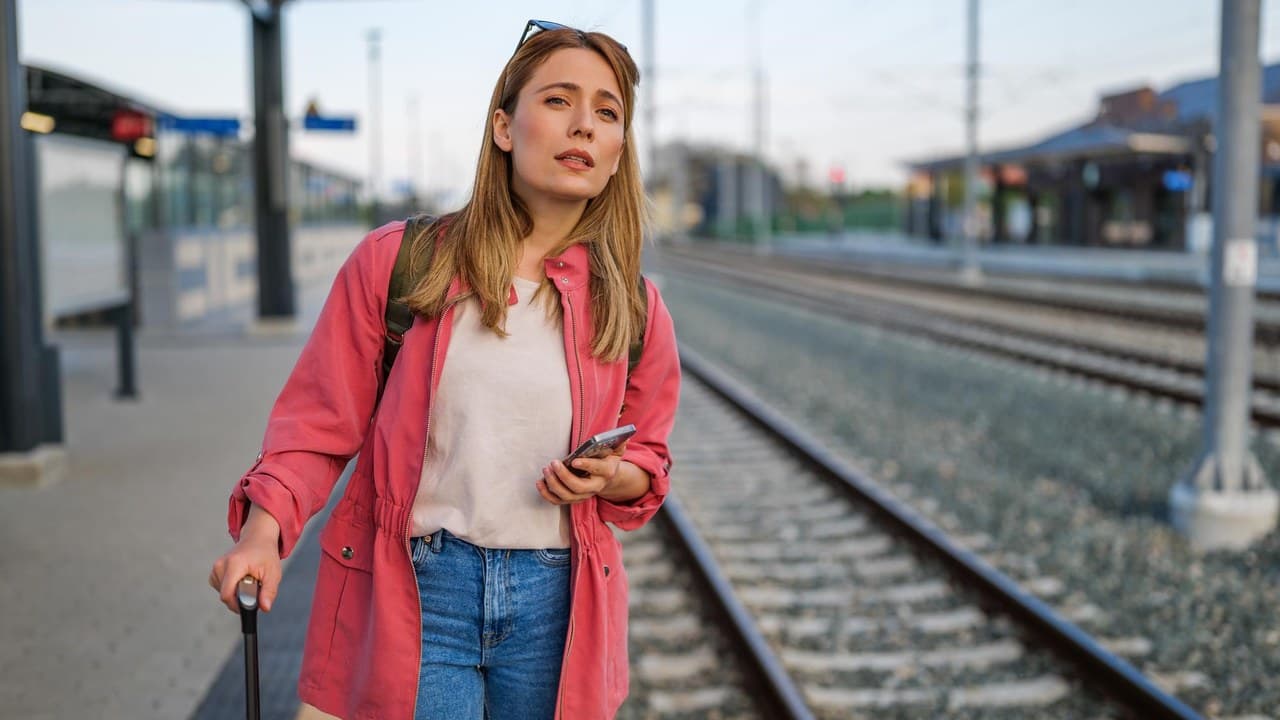 Egy nő áll a vasútállomáson, bőrönddel és telefonnal, aggódva néz fel.