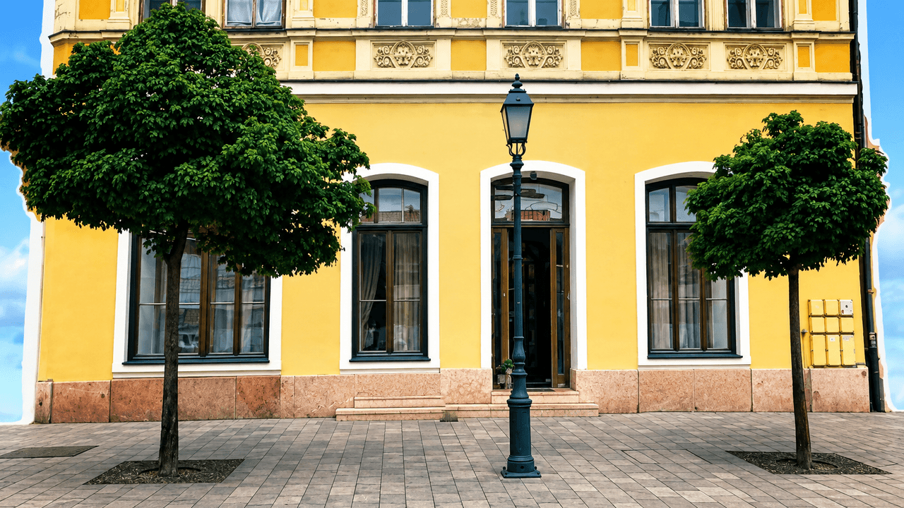 Igéző sárga színházépület két fával és lámpással, bábszínházra utalva.