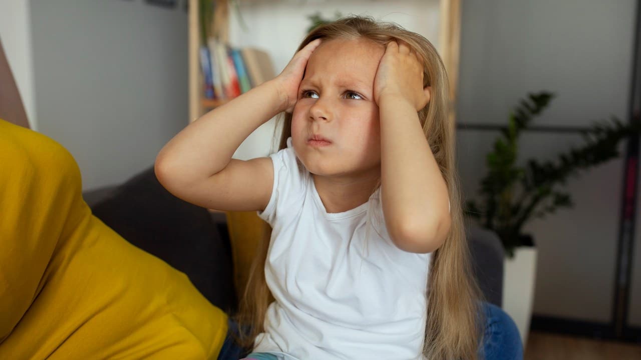 Zavart kislány fogja a fejét, ami figyelemzavarral vagy stresszel kapcsolatos lehet.