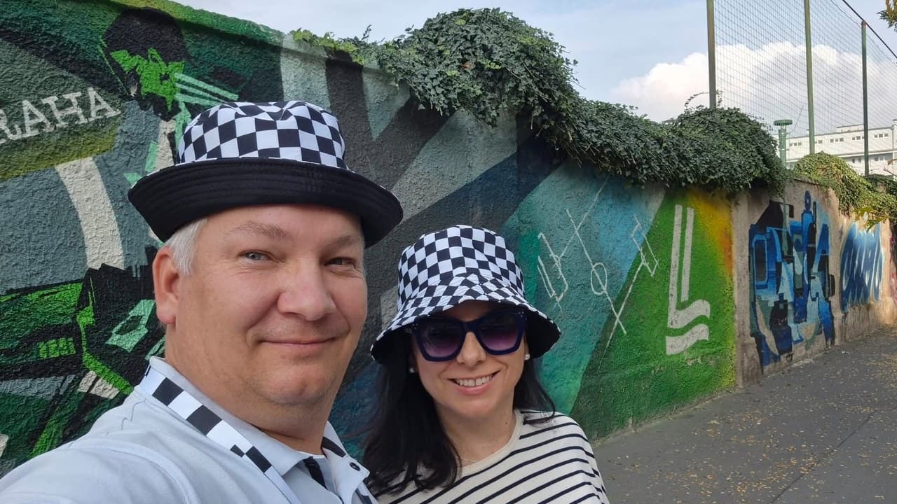 A Thermowhite 10-es csapat két tagja kockás kalapban mosolyog graffitis fal előtt.